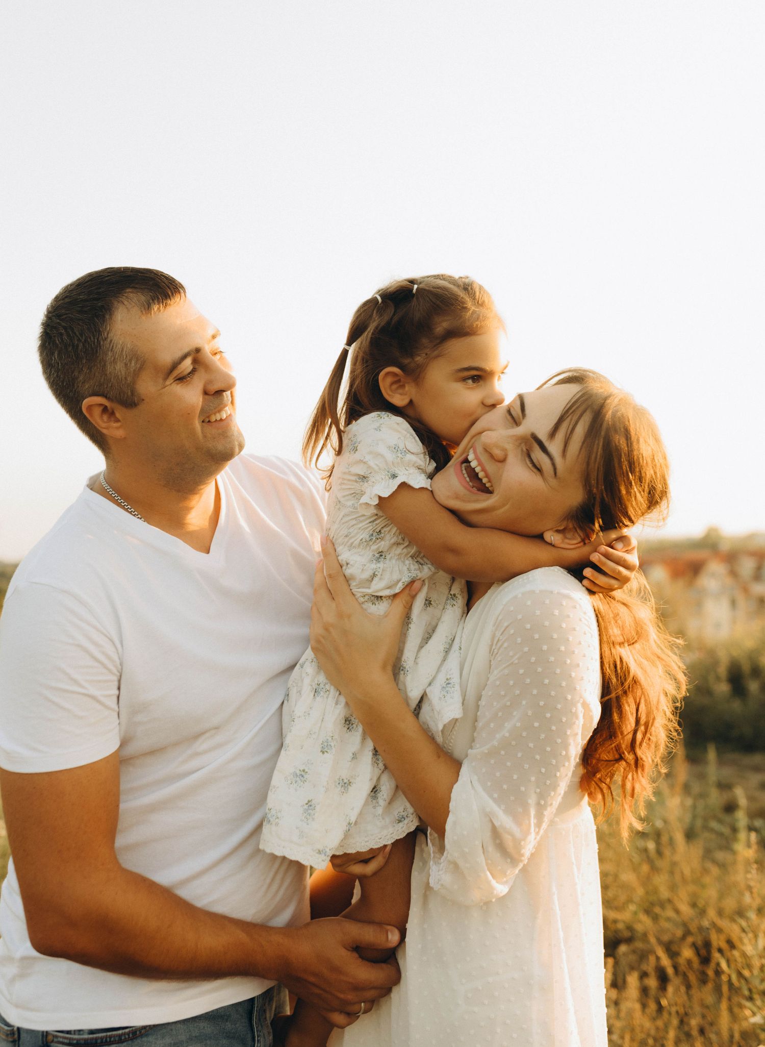 Parents embracing their young daughter in warm evening sunshine